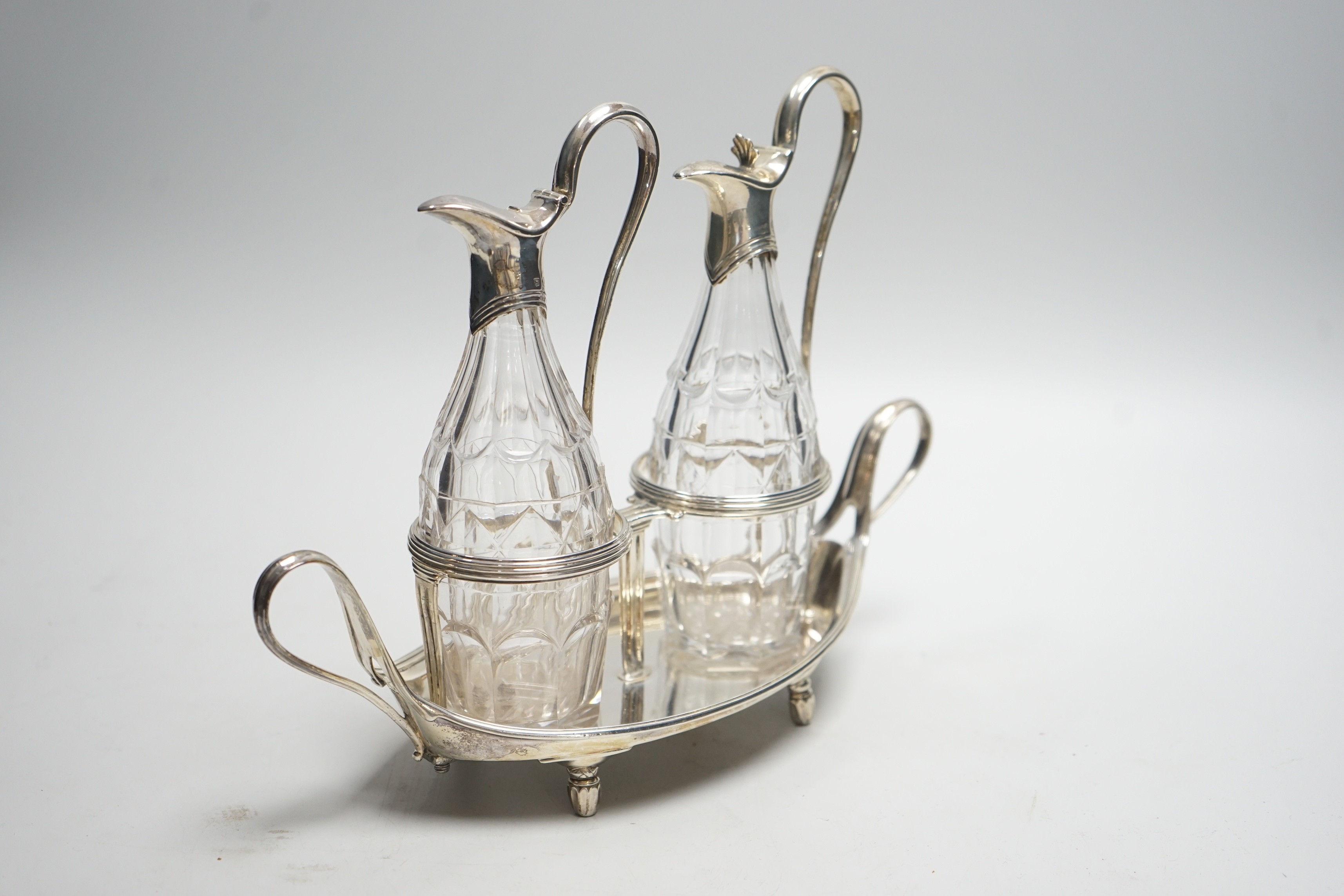 A George III silver navette shaped two handled oil and vinegar stand, with two matching silver mounted cut glass bottles (one thumbpiece missing), John Scofield, London, 1787, length 28cm, stand, 13.7oz.